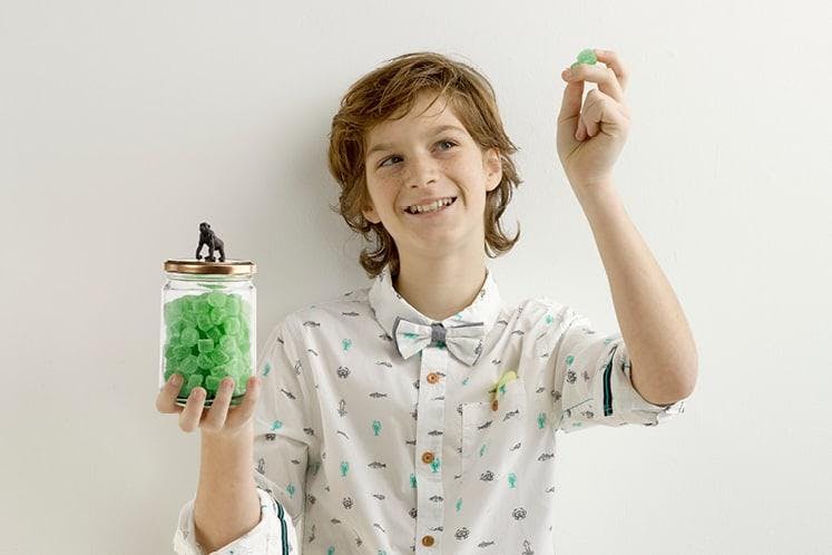 Jongen in communiekledij met glazen bokaal gevuld met groene snoepjes